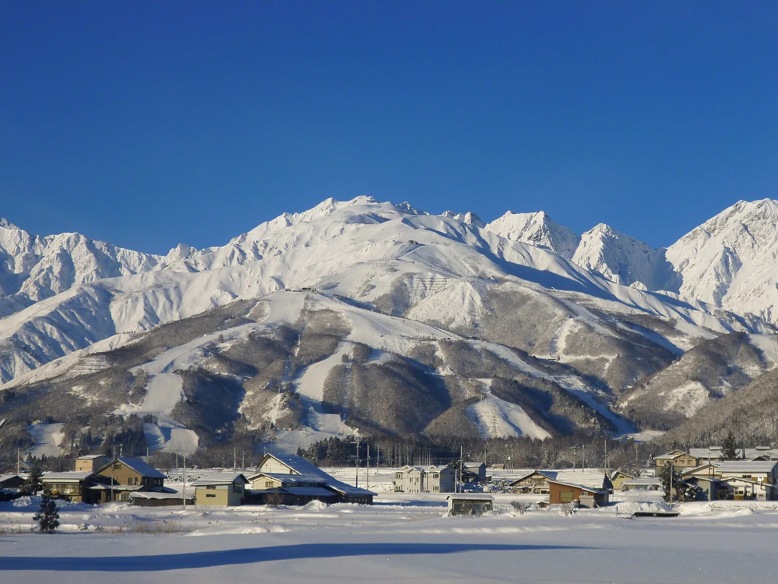 The snow-covered peaks and ski runs of the Hakuba Valley in the Japanese Alps above a village.