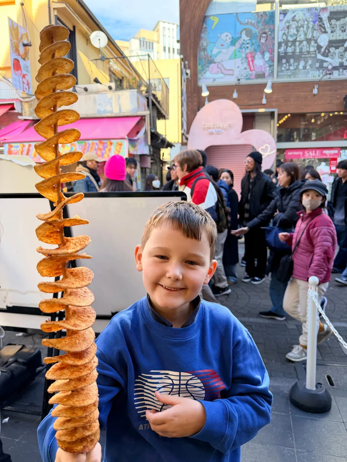 A child holds a spiral tornado potato on a stick on a Harajuku street in Tokyo.