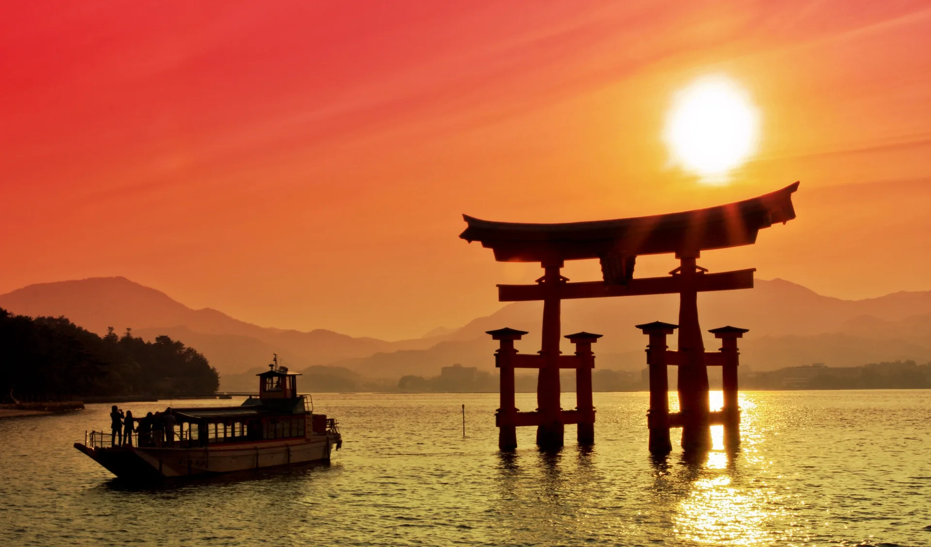 The great vermilion “floating” torii gate of Itsukushima Shrine at Miyajima silhouetted against a glowing sunset, with a boat passing behind.