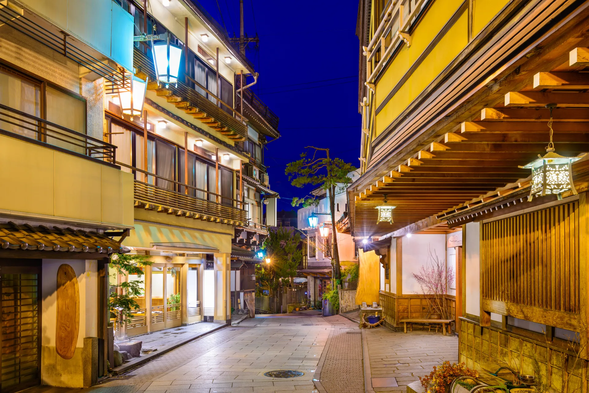 A traditional onsen-town street lined with wooden ryokan inns and glowing lanterns at dusk.