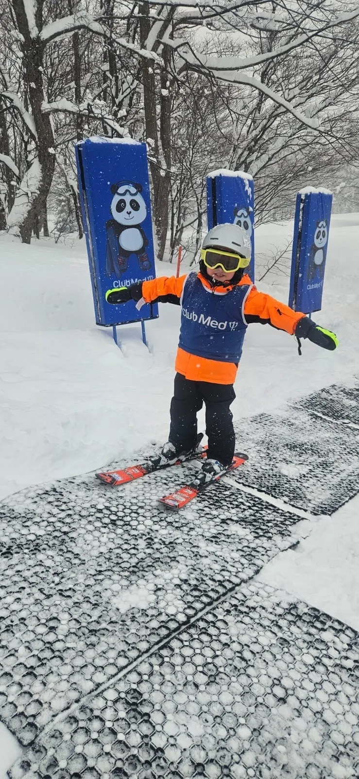 A young child in ski gear on the beginner magic-carpet lift at a Japanese ski resort.